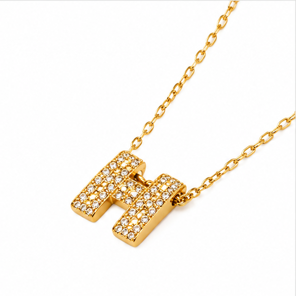 : High-angle view of Zafiroon gold-plated initial H charm necklace showcasing the glossy finish and modern geometric design on a clean white background.