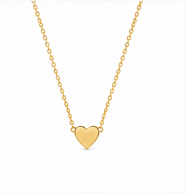 A delicate gold chain necklace with a small polished heart pendant, arranged elegantly on a textured white fabric background surrounded by bright white baby's breath flowers under warm, soft lighting.