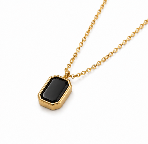 Premium gold link chain necklace with a black emerald cut gem medallion resting on a seamless white backdrop.