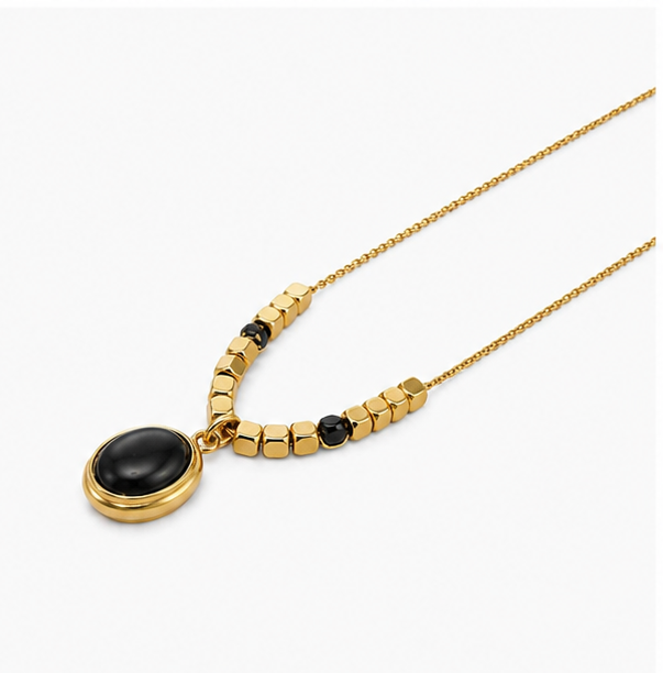 Wide angle shot of a minimalist gold necklace with square block beads and a black oval medallion lying on a seamless background.