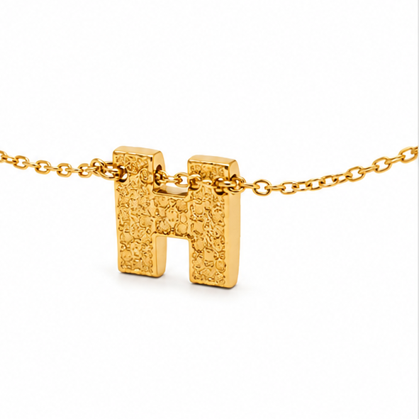 Backside view of Zafiroon gold initial H pendant necklace revealing a unique textured hammered metal pattern on a plain white background.