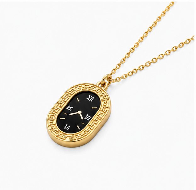 High angle perspective shot of Zafiroon black and gold oval clock necklace resting on a seamless white surface.