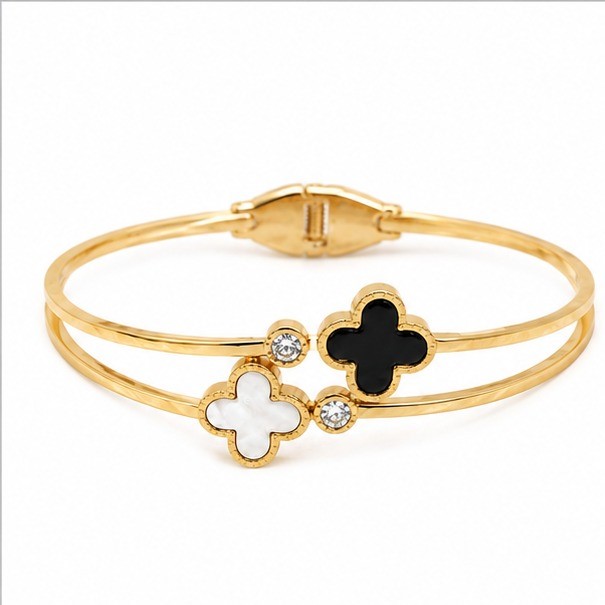 Gold plated stainless steel split band hinged bangle bracelet displaying alternating black enamel and white pearl clover motifs with clear crystal discs on a white background