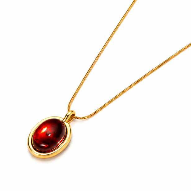 High angle left perspective of a premium gold plated necklace with a deep red oval gemstone medallion on a white background.