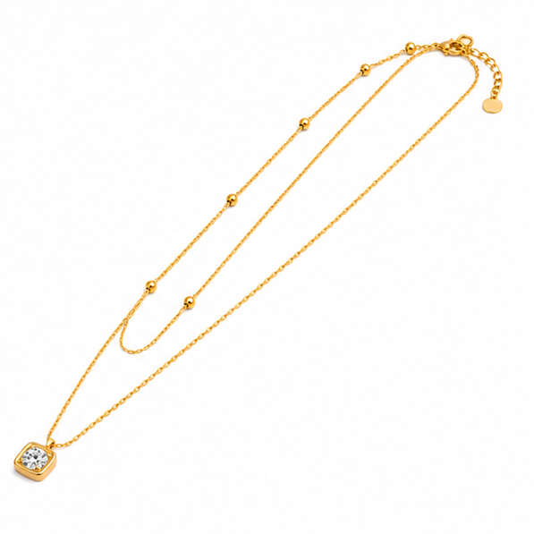 Low angle studio perspective of a golden double strand satellite necklace highlighting a minimalist clear solitaire square pendant.