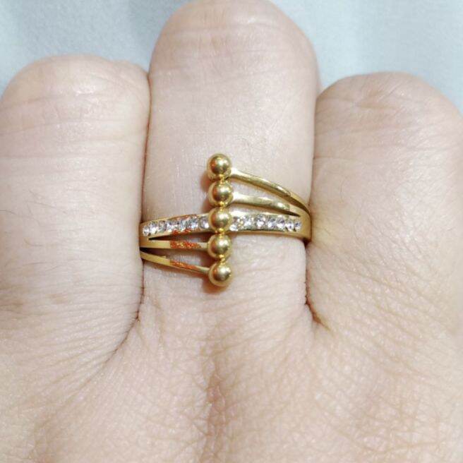 Gold plated stainless steel multi layer cross over statement ring featuring vertical gold beads and cubic zirconia crystals on a light background